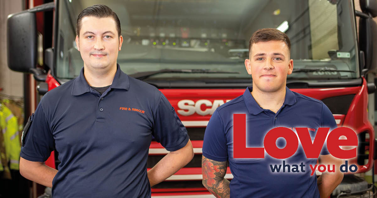 Two firefighters, in work uniform, in front of a fire engine 