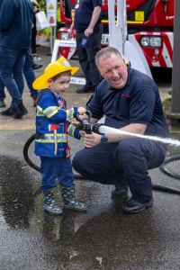 Child dressed as firefighter being shown how to use hose reel