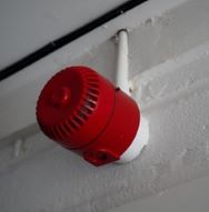 a red fire safety sounder on a white wall