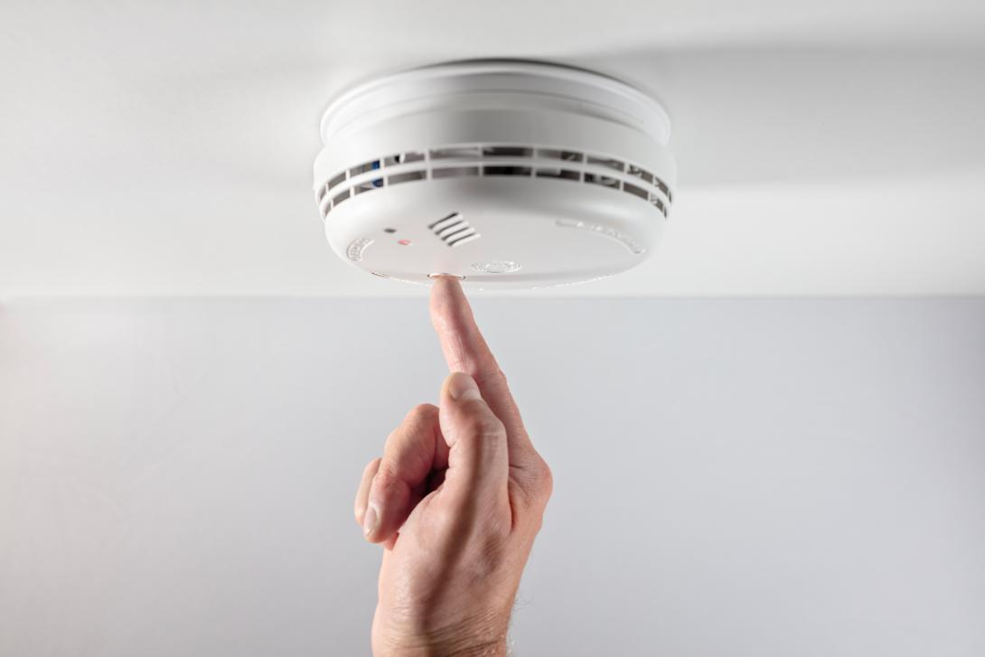 finger pressing smoke alarm to test it