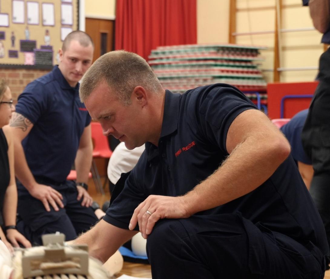 A firefighter helping teach CPR skills at a school