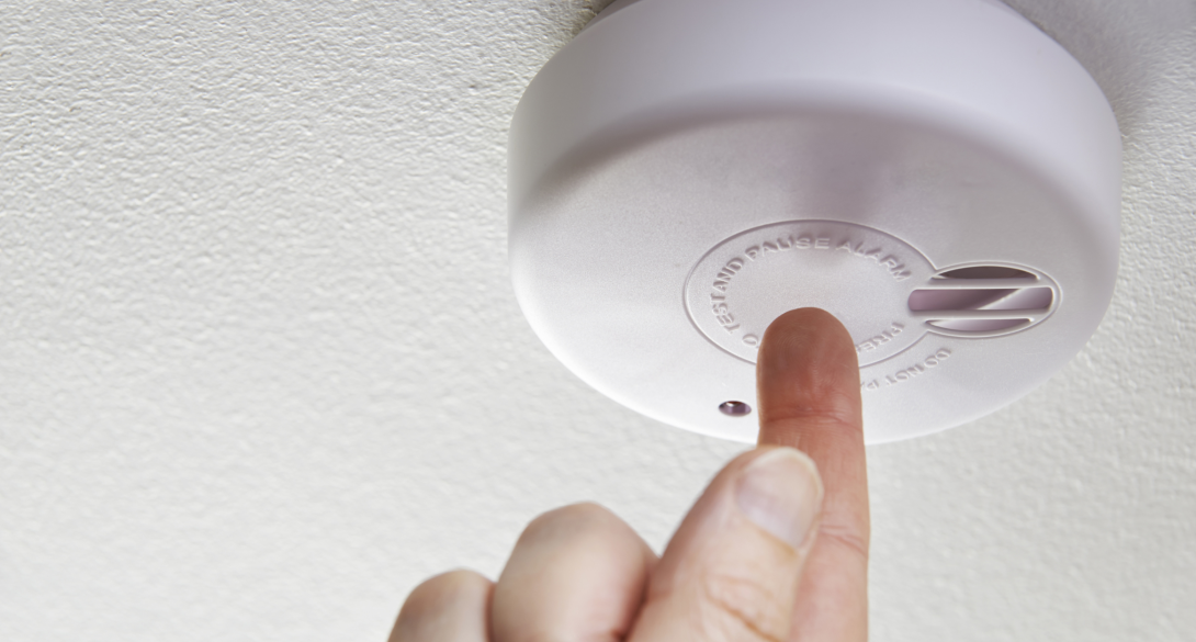 person pressing the test button on the smoke alarm