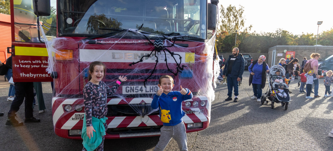 Two young children standing in front of a fire engine with Halloween decorations on it